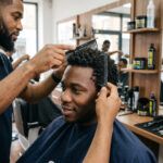 Barber combing through textured curls with a wide-tooth Comb-Thru comb, Pro-Line Comb Thru jars on the shelf behind
