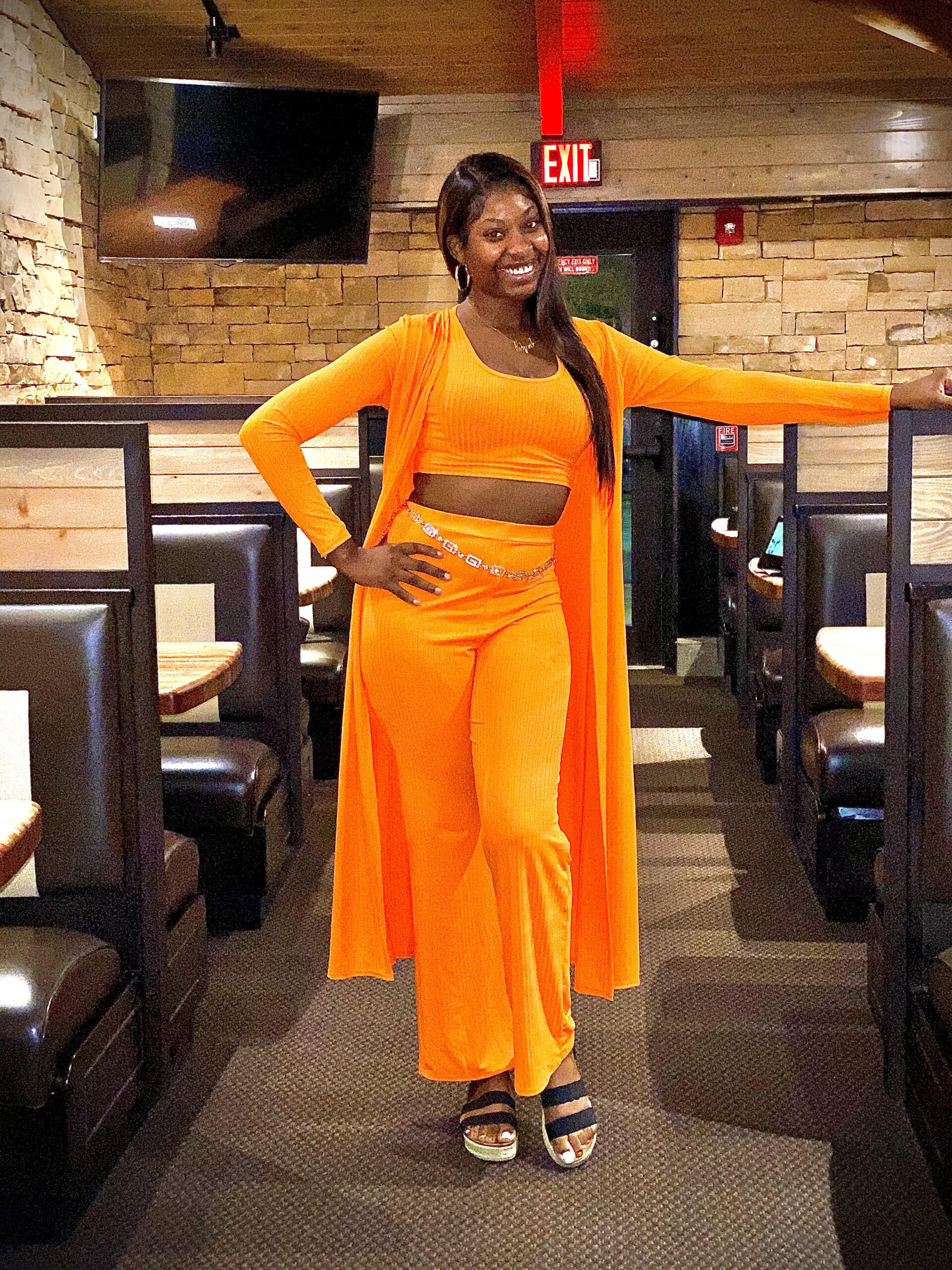 Fashion creator Erykah in a bright tangerine-orange three-piece set with a ribbed crop top, wide-leg pants, and a long duster cardigan